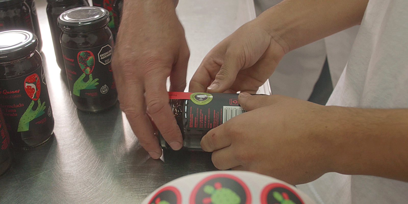 Manos colocan etiquetas en un frasco de mermelada de tuna Las Quinas. Diseño por Tridimage.