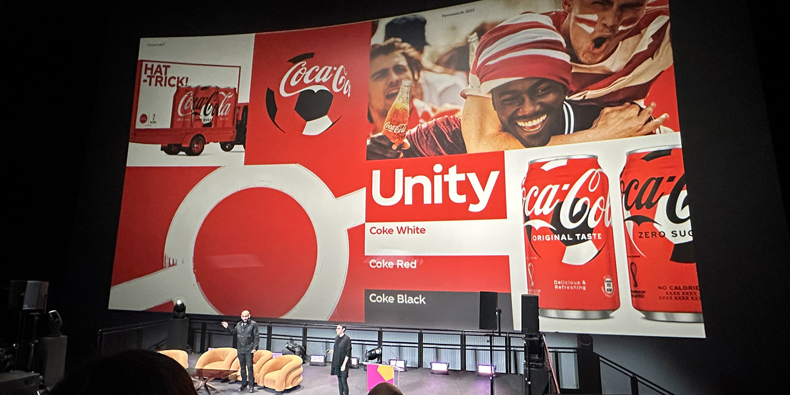 Un hombre y una mujer en el escenario con una pantalla grande que muestra recursos de diseño de Coca Cola.