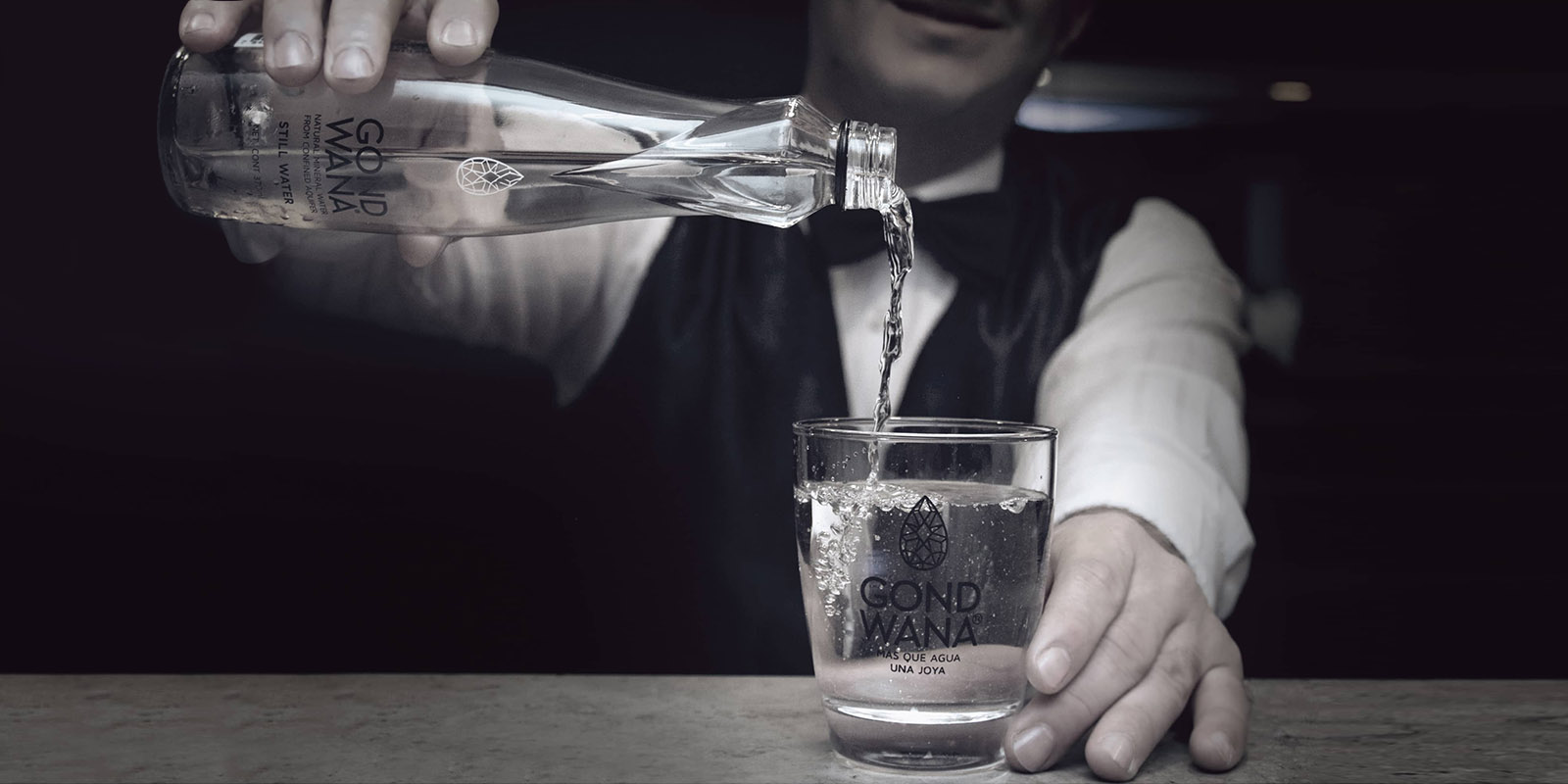 Un hombre vierte artísticamente agua mineral premium Gond Wana en un vaso.