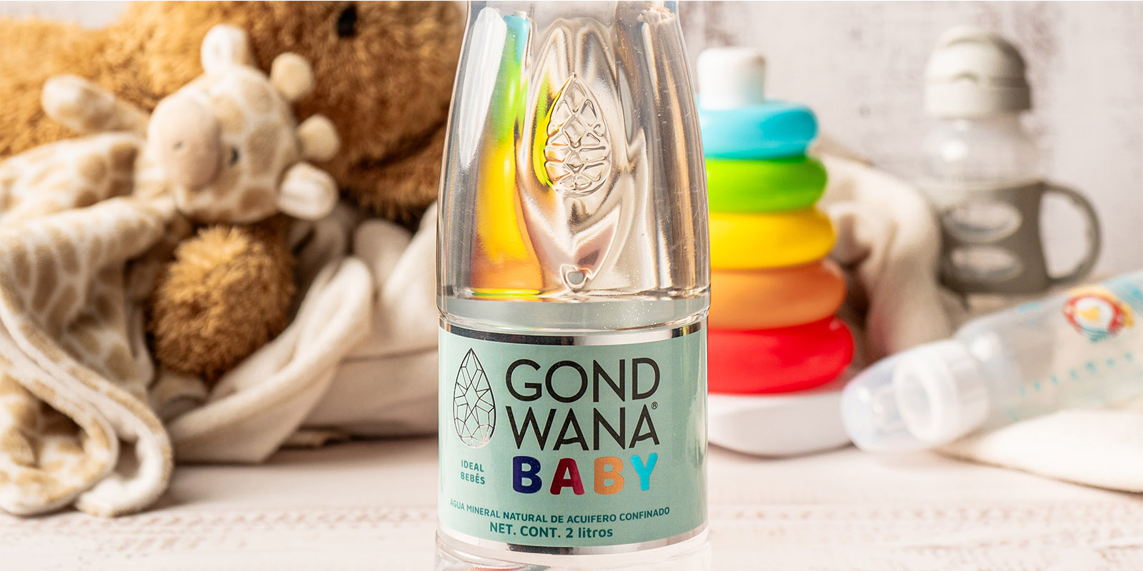Una botella de agua mineral premium Gond Wana Baby, al lado de un osito de peluche y juguetes de bebé, diseño de packaging por Tridimage.