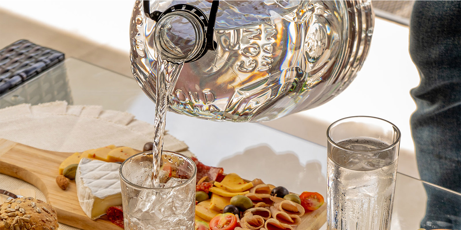 Una persona vierte agua mineral premium Gond Wana envasada en bidón en vasos sobre una mesa servida con una picada, diseño de packaging por Tridimage.