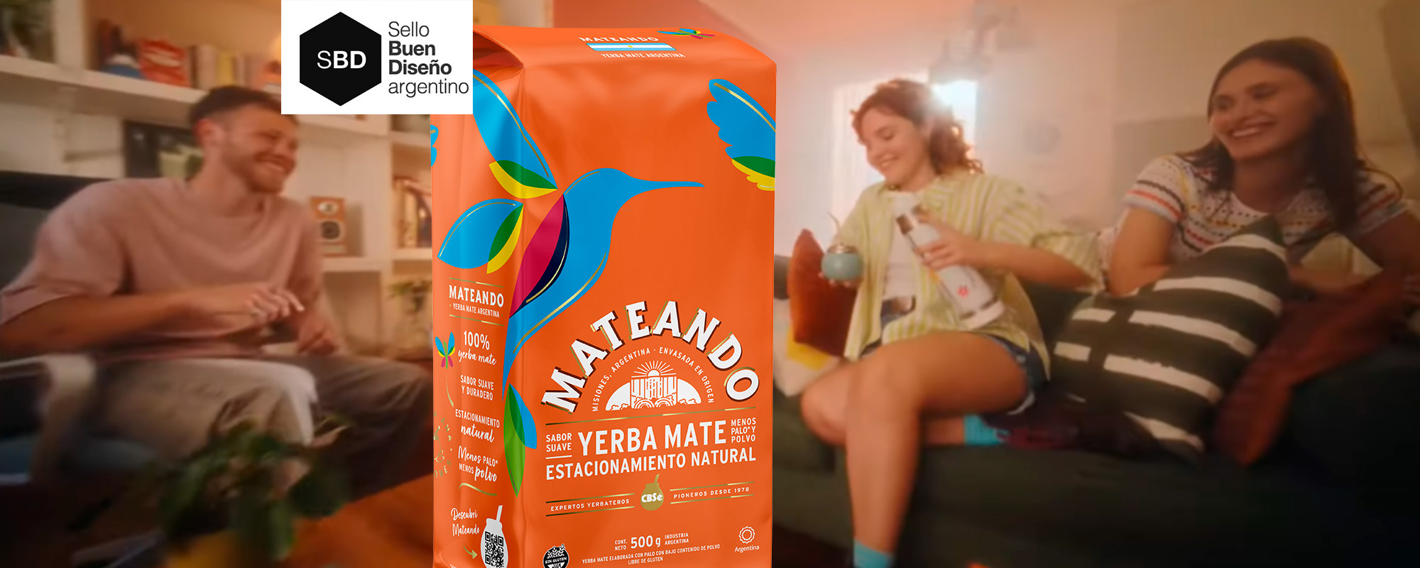 Grupo de jóvenes riendo y compartiendo un mate en una sala de estar, con un paquete de yerba Mateando en primer plano, destacando su diseño colorido y natural. Diseño de packaging por Tridimage. Sello Buen Diseño Argentino