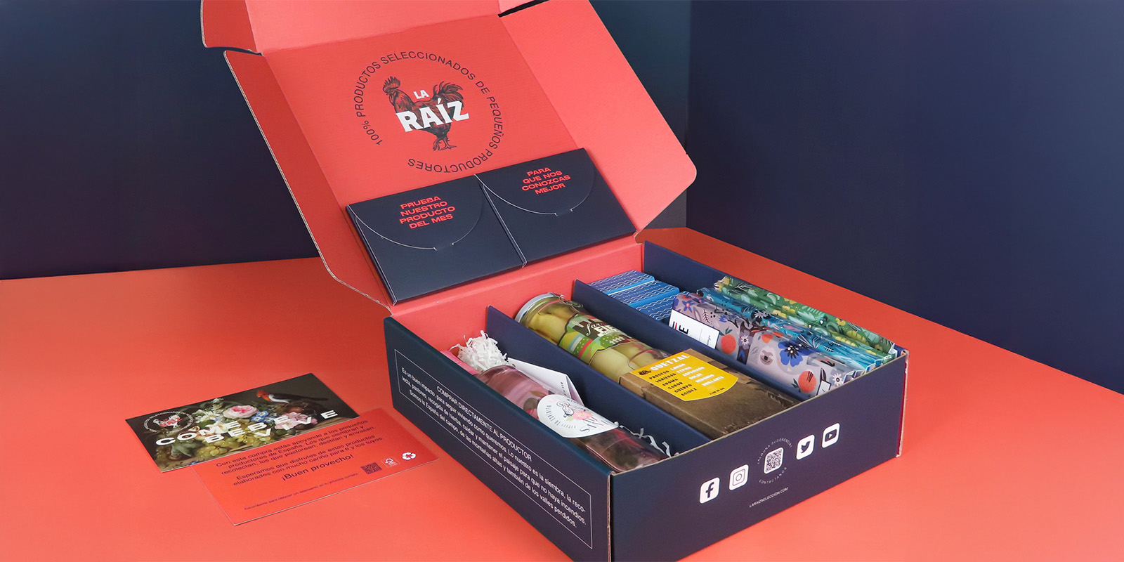 Caja de degustación premium La Raíz con productos de pequeños productores: caja abierta con compartimentos organizados, mostrando frascos, paquetes y tarjetas informativas. La tapa interior tiene el mensaje “100% PRODUCTOS SELECCIONADOS DE PEQUEÑOS PRODUCTORES” junto al logo de un gallo. En el exterior, hay tarjetas con información sobre los beneficios de los productos y un QR para más detalles.