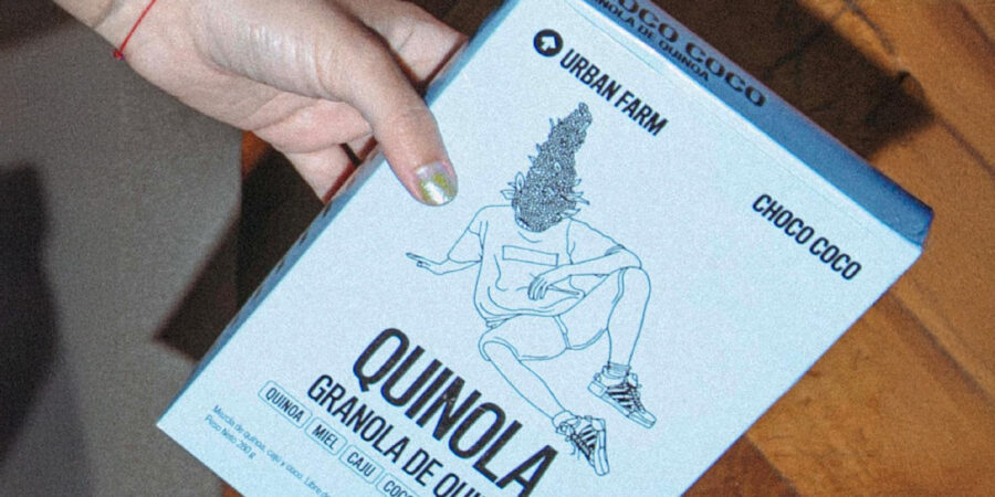Persona sostiene caja de “Quinola Choco Coco” Urban Farms con diseño freak estilo Gen Z: ilustración excéntrica en estilo lineal de un personaje hecho de granos de quinoa. El empaque de color plano vibrante resalta ingredientes naturales.