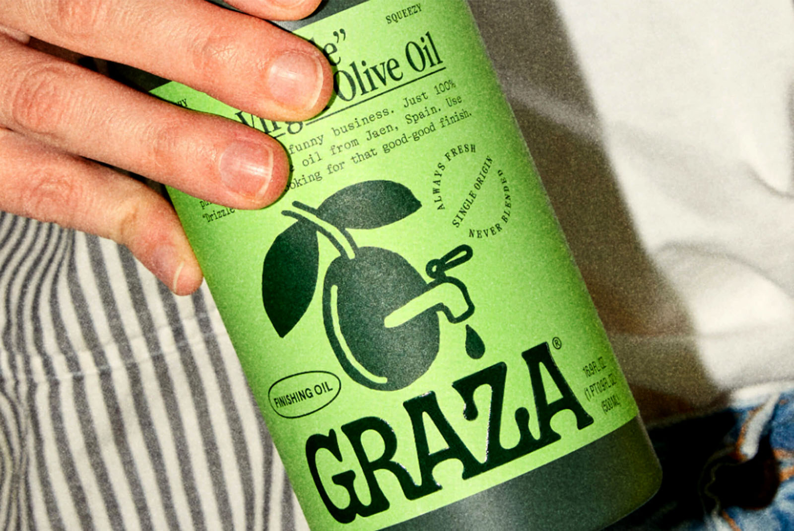 Diseño de packaging freak: el aceite de oliva de Graza adopta un envase anticonvencional con un formato de botella exprimible y una etiqueta verde eléctrico con texto estilo máquina de escribir e ilustraciones dibujadas a mano. El diseño rechaza la categoría de aceite de oliva premium. Diseño de Gander.