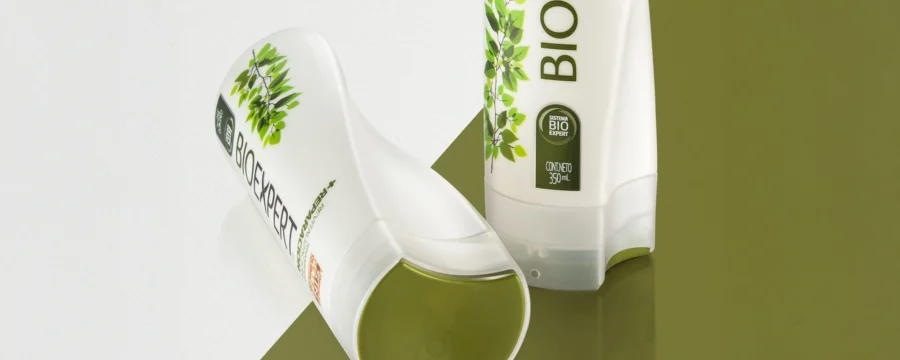 Dos botellas de shampoo BIOEXPERT con diseño estructural desarrollado por Tridimage. Una está de pie y la otra acostada, ambas blancas con detalles verdes y gráficos de hojas que refuerzan el concepto natural. El envase integra forma y mensaje, con líneas suaves y ergonómicas que comunican sustentabilidad y cuidado personal.