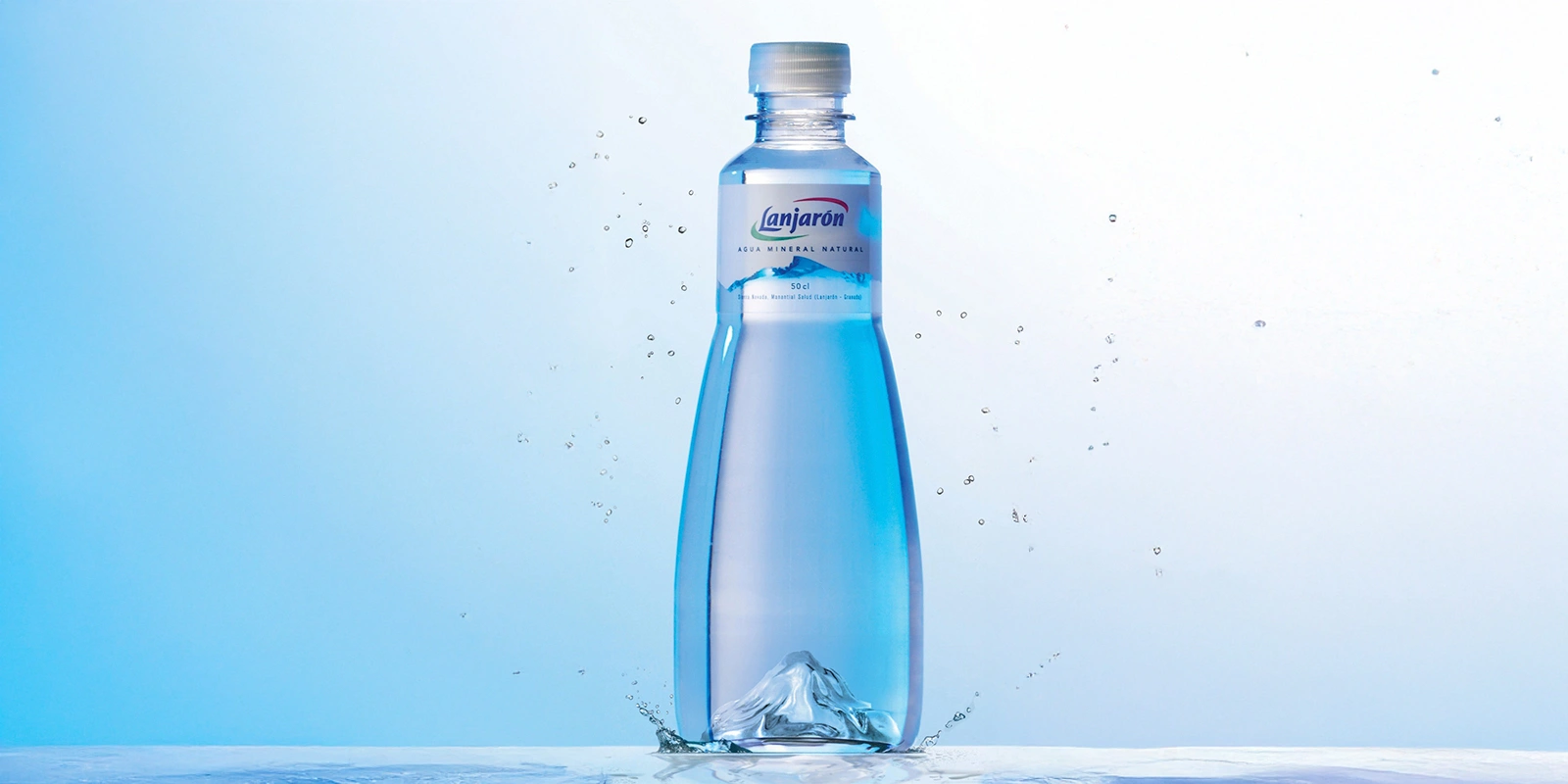 Botella de agua mineral Lanjarón diseñada por Tridimage, con forma estilizada y tintes azules que evocan frescura. El envase de 500 ml está rodeado por salpicaduras de agua, reforzando la idea de pureza. La etiqueta destaca el origen natural del producto, envasado en el Parque Natural Sierra Nevada, y el diseño transmite elegancia y conexión con el entorno.