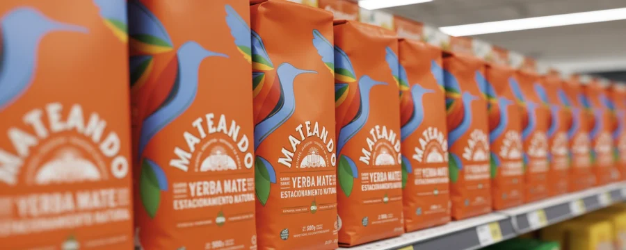 Primer plano de bolsas de yerba mate Mateando de color naranja con un pájaro azul, alineadas en la estantería del supermercado.