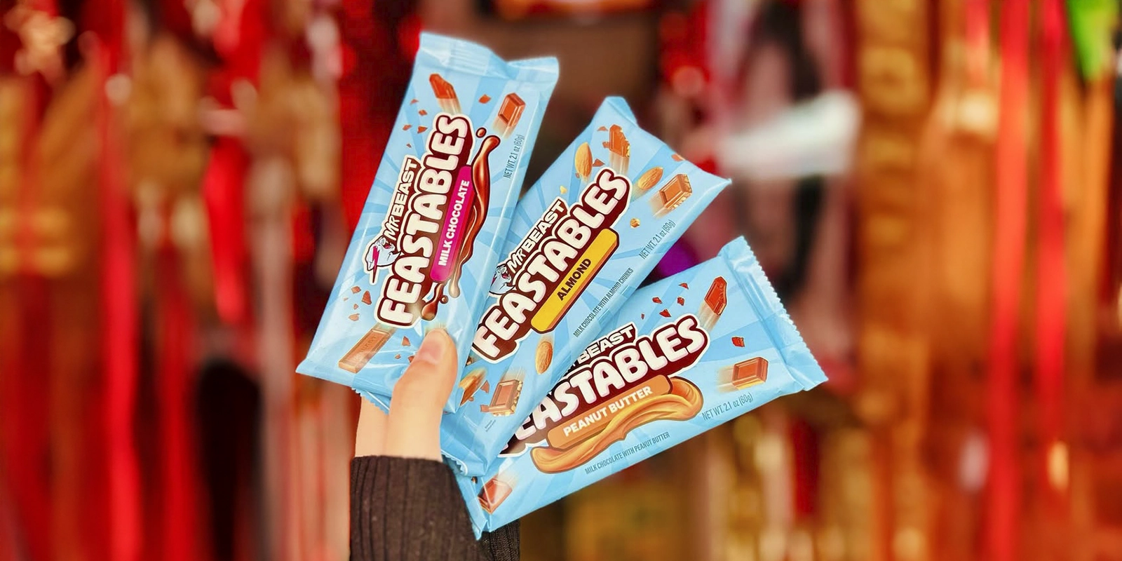 Tabletas de chocolate Feastables de MrBeast en envoltorios azul brillante con sabores Milk Chocolate, Almond y Peanut Butter. Ejemplo de consistencia de color de marca.