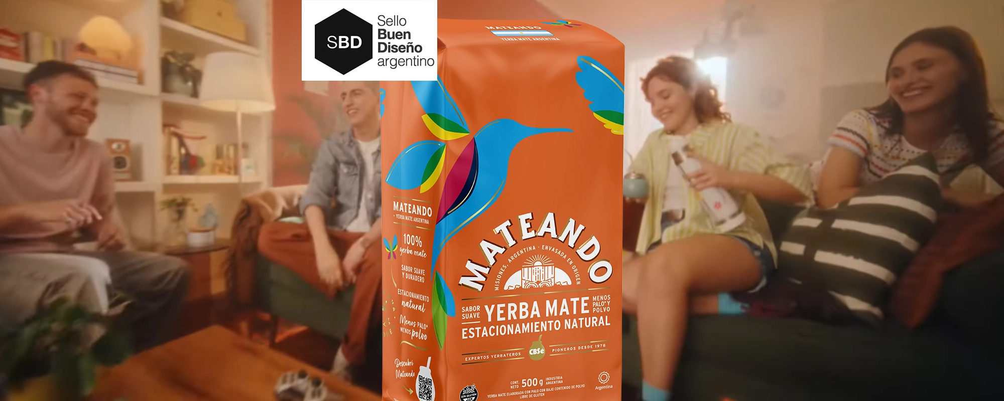 Grupo de jóvenes riendo y compartiendo un mate en una sala de estar, con un paquete de yerba Mateando en primer plano, destacando su diseño colorido y natural. Diseño de packaging por Tridimage. Sello Buen Diseño Argentino