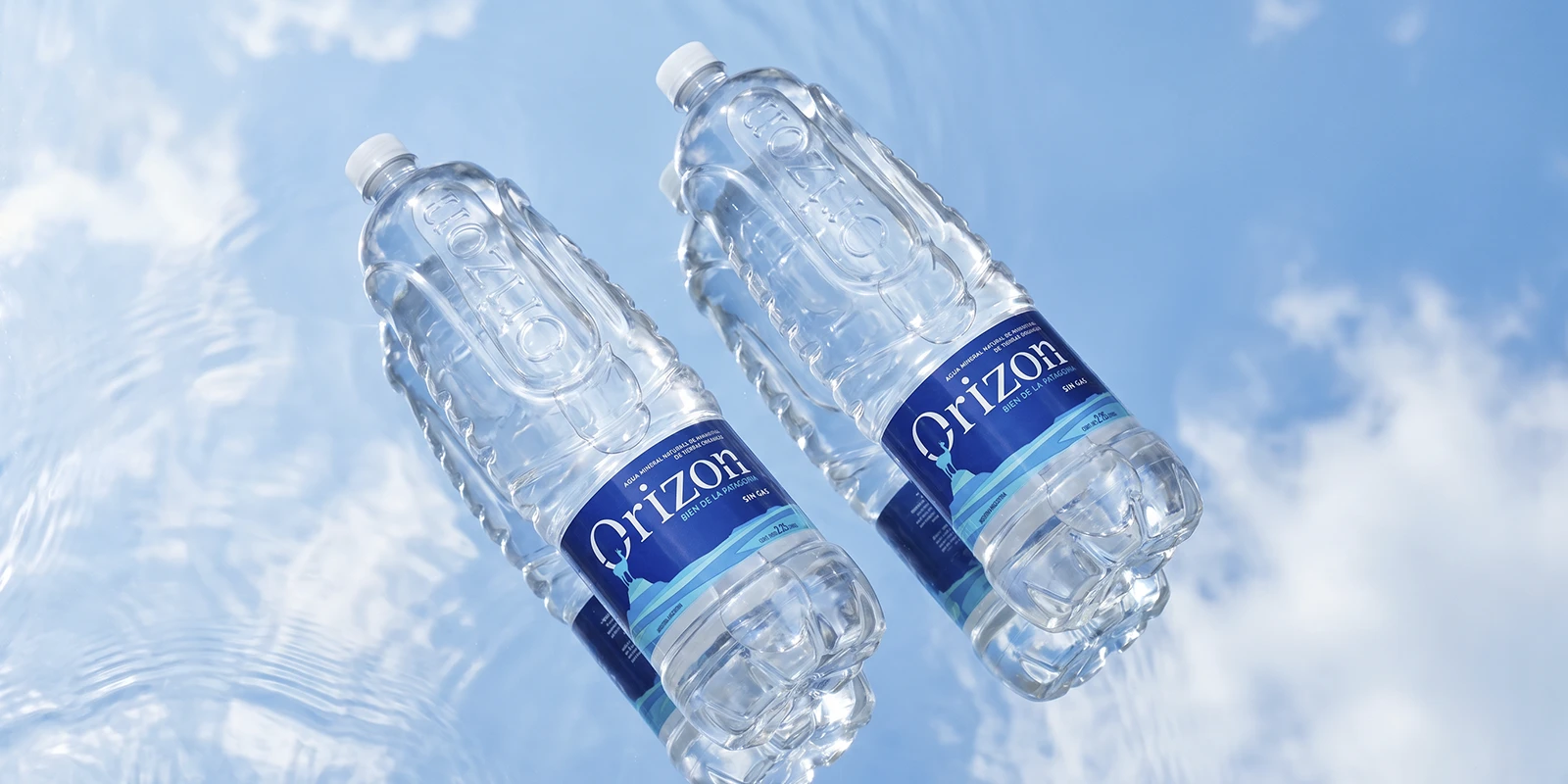 Dos botellas de agua mineral Orizon de perfil sobre una superficie de agua cristalina con reflejos celestes.