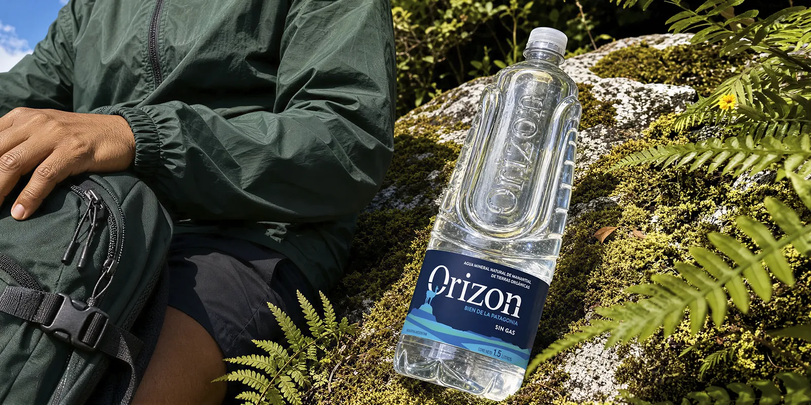 Botella de agua mineral Orizon de 1.5 litros descansando sobre una roca con musgo junto a un senderista.