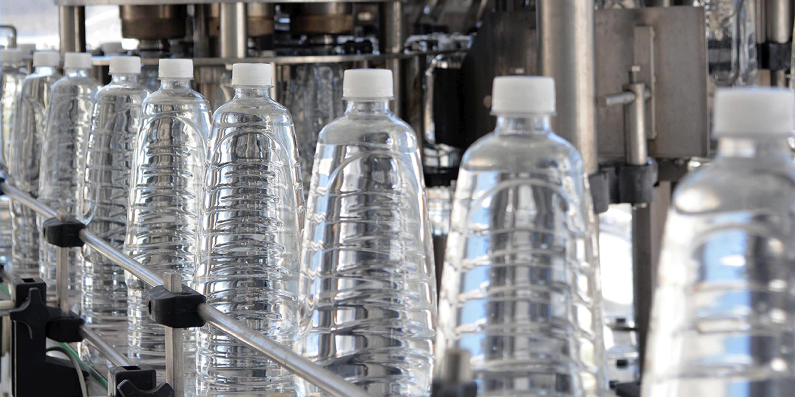 Fila de botellas plásticas de agua Orizon sin etiqueta avanzando por una cinta transportadora en la planta de producción.