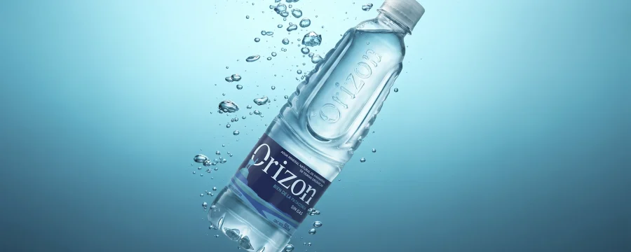 Botella de agua mineral Orizon flotando bajo el agua con burbujas, destacando su etiqueta azul y diseño estructural.