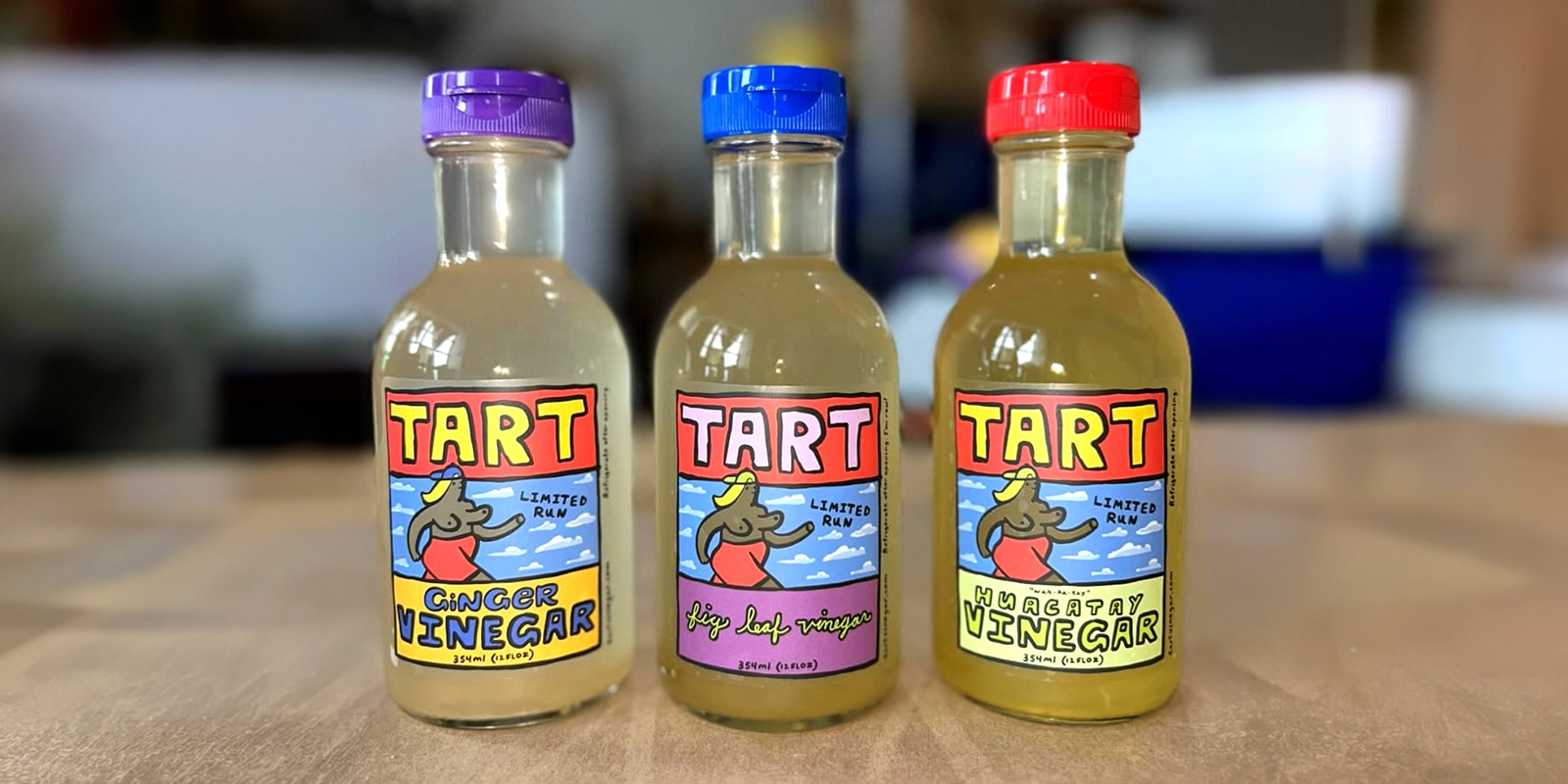 Tres botellas de vinagre Tart con etiquetas ilustradas de ginger vinegar, fig leaf vinegar y huacatay vinegar.