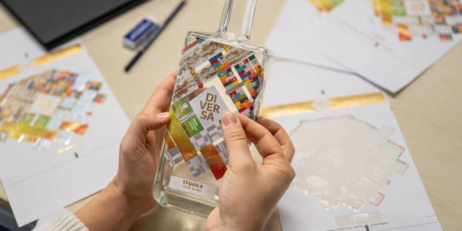 Aplicación manual de etiqueta con acabados holográficos y stamping sobre botella de vidrio de Tequila Diversa.